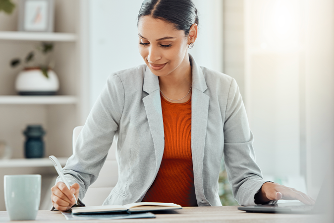 Smiling young woman studying with book, pen and laptop