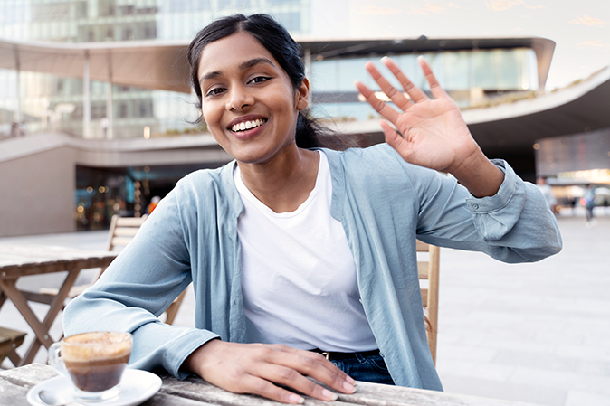 Young south asian woman on campus smiling and waving with cup of chai