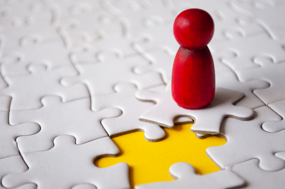 Image of a small wooden doll on a puzzle piece, about to be slotted into a puzzle gap