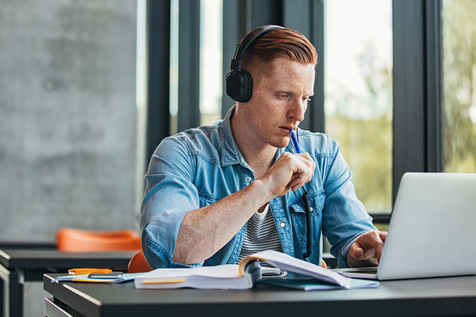 Young man wearing headphones while studying in front of a laptop