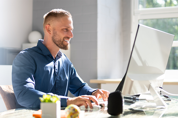 Young man smiling while typing on a laptop at his desk at home