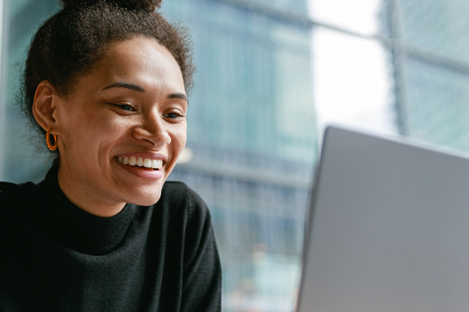 Young woman smiling in front of a laptop next to a big window